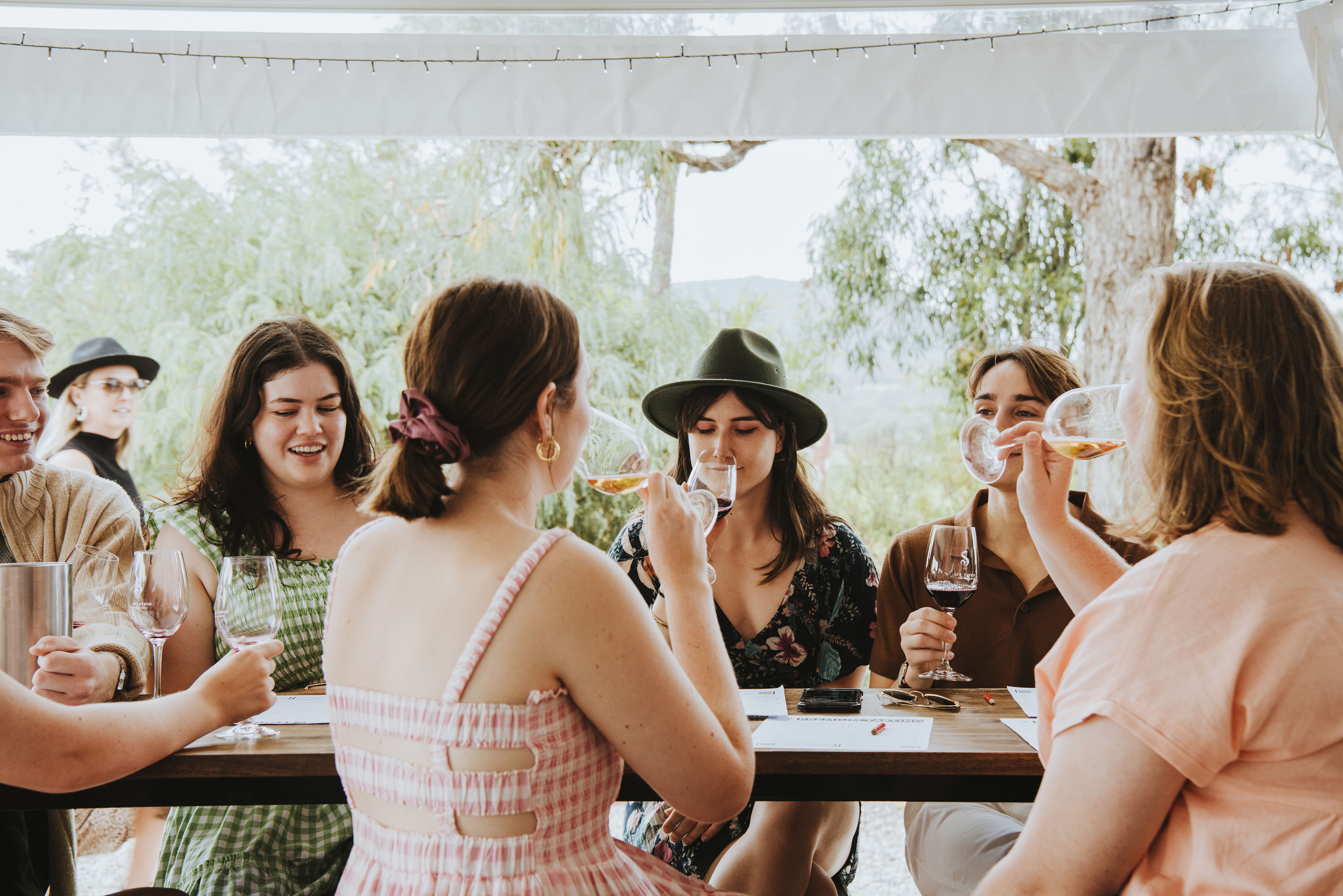 People seated on a long table doing a wine tasting outside